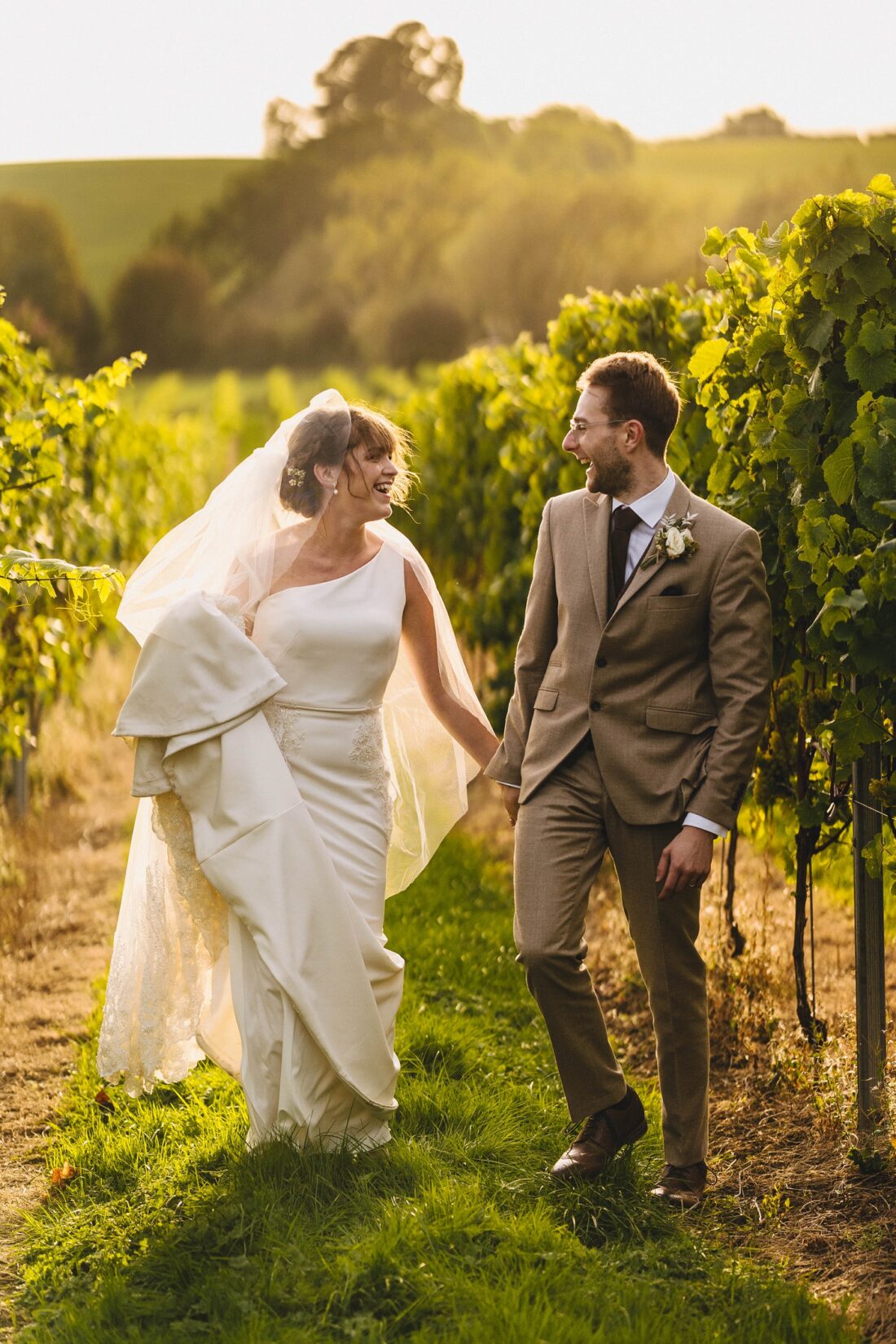 bride and groom laughing and walking among the grape wines