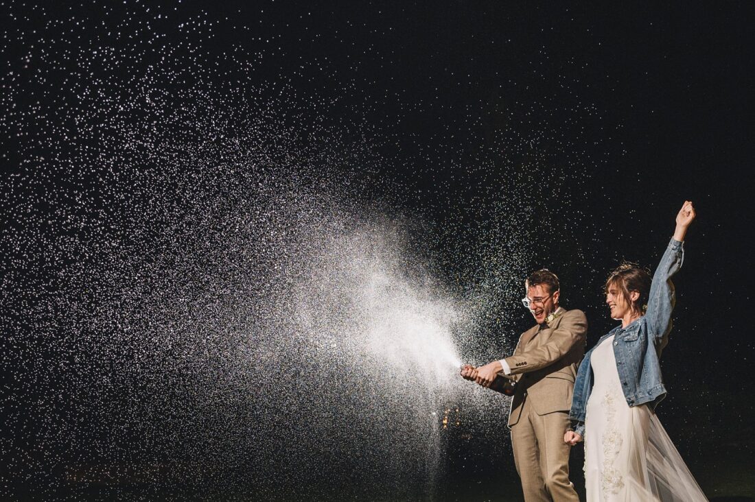 groom opening the champagne at night and bride cheering