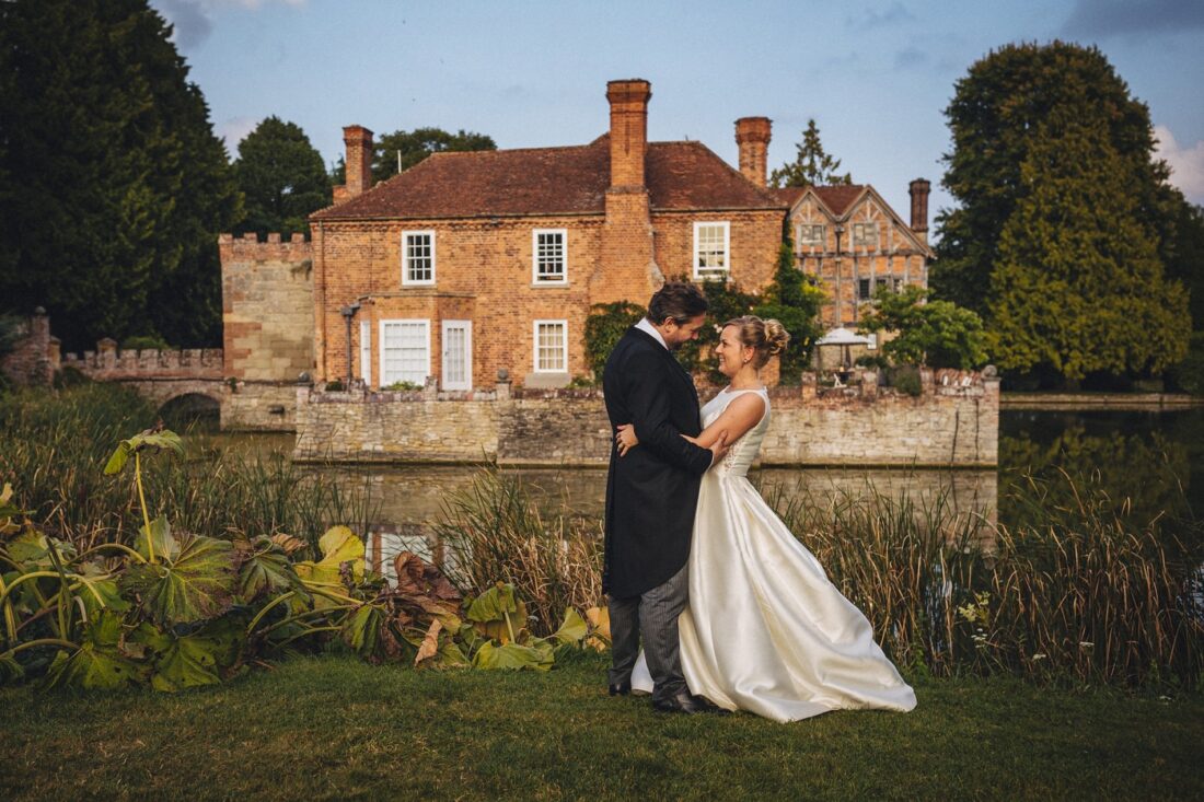 bride and groom standing together in front of the house and moat at Birtsmorton Court