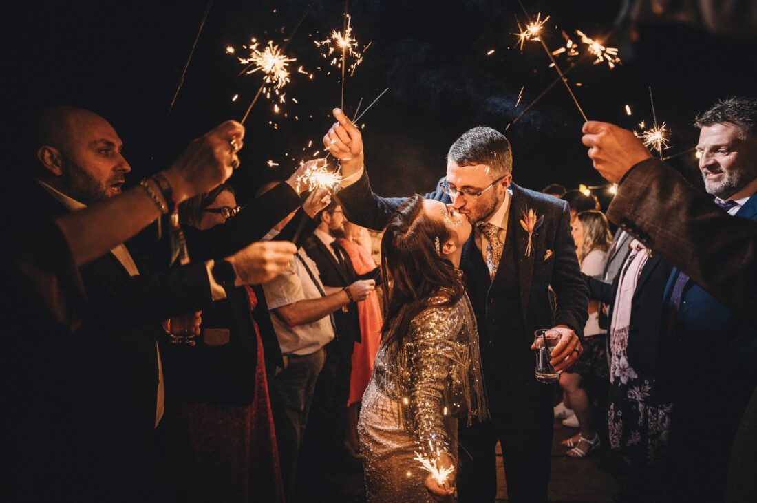 bride and groom kissing under the sparklers surrounded by guests