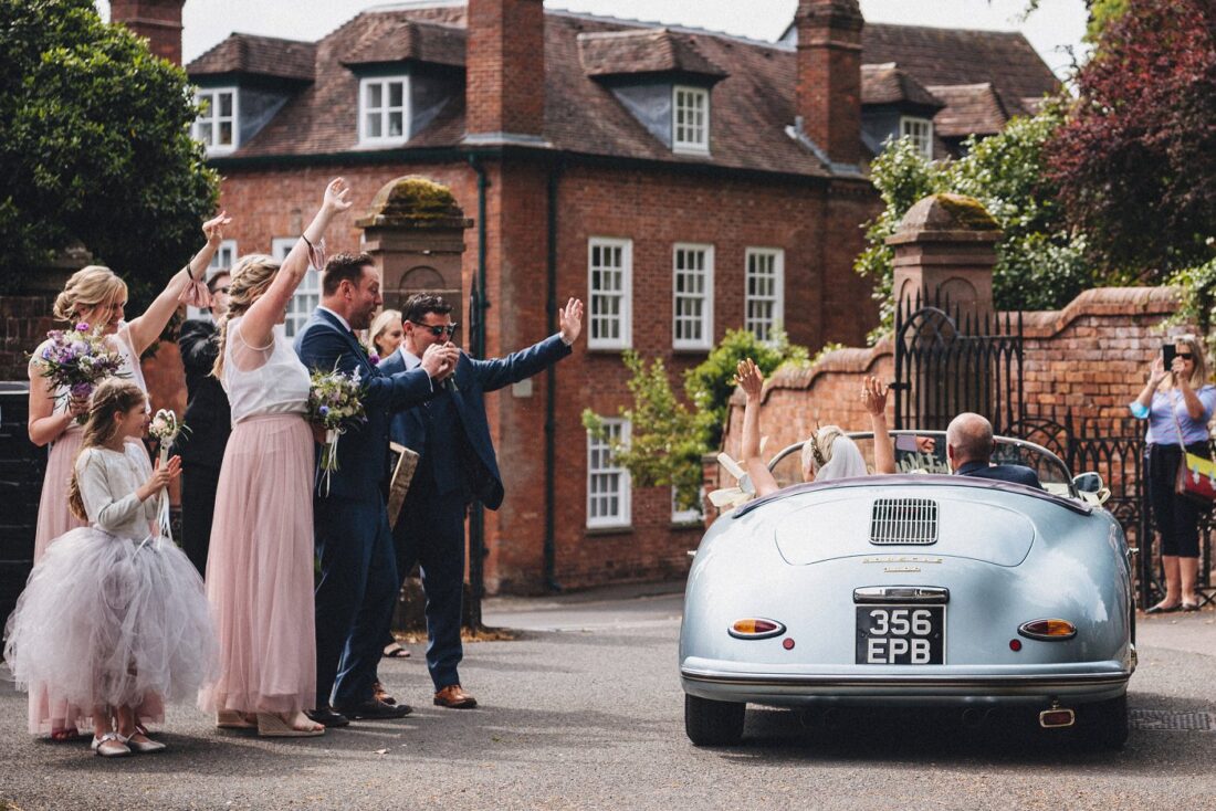 just married couple leaving the church in their car and guests waving at them Eastnor