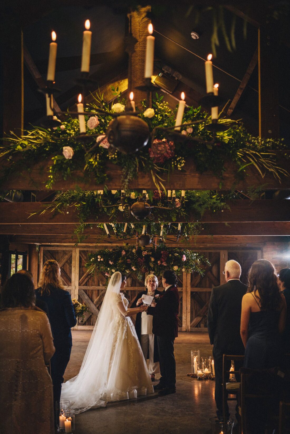 shamanic ceremony under the chandeliers and flowers in the wainhouse at Dewsall Court, bride and groom holding hands