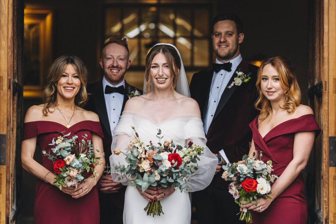 bride bridesmaids and bridesmen posing for the group photo in the main entrance at Dewsall Court 