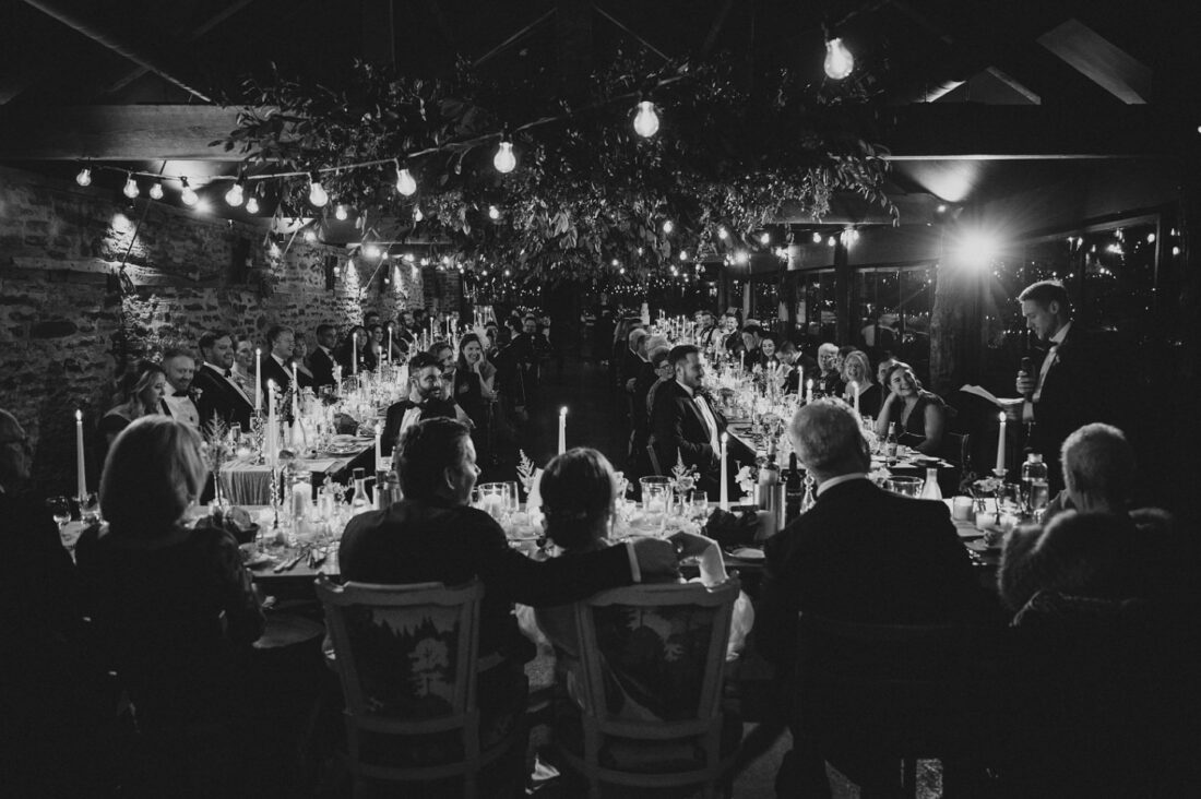 best man doing his speech at the wainhouse at Dewsall Court, couple and the top table in the foreground, candles and guests in the background