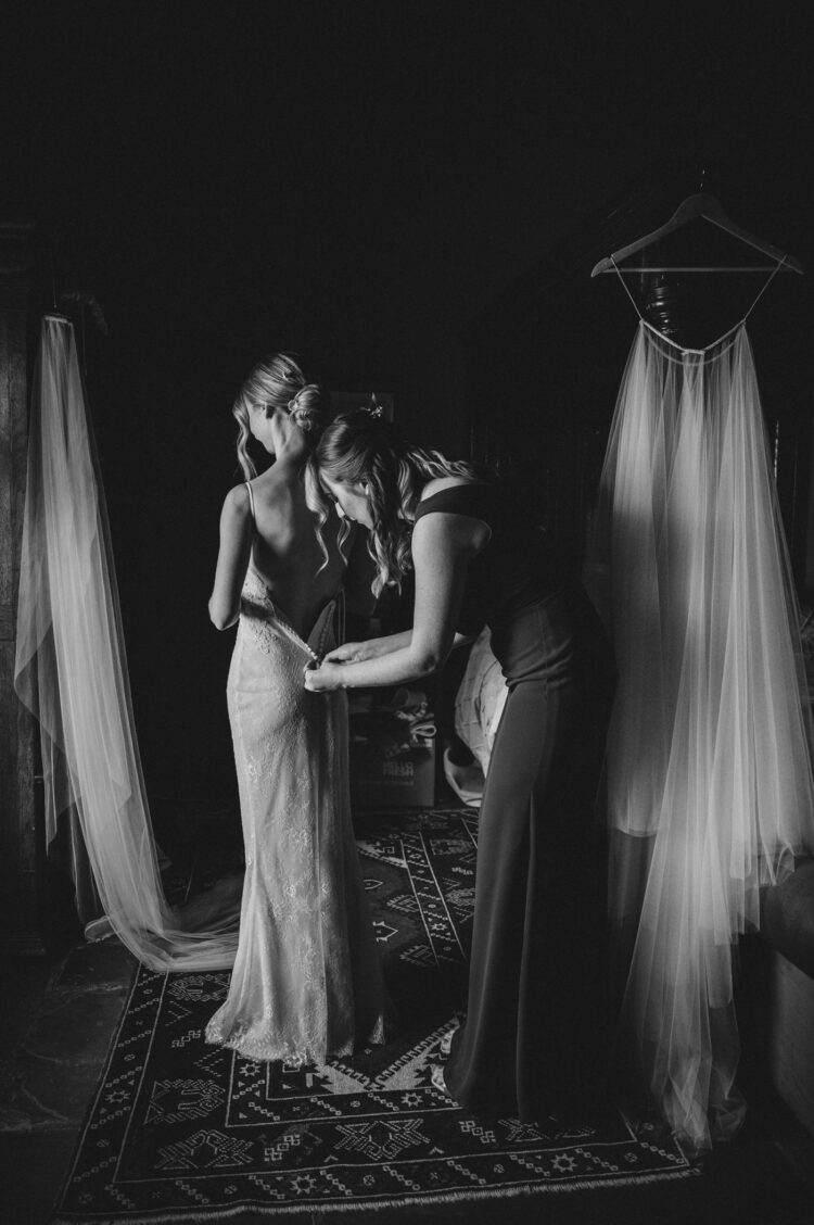 a bridesmaid helping a bride to get into a wedding dress at Old Downton Lodge Ludlow