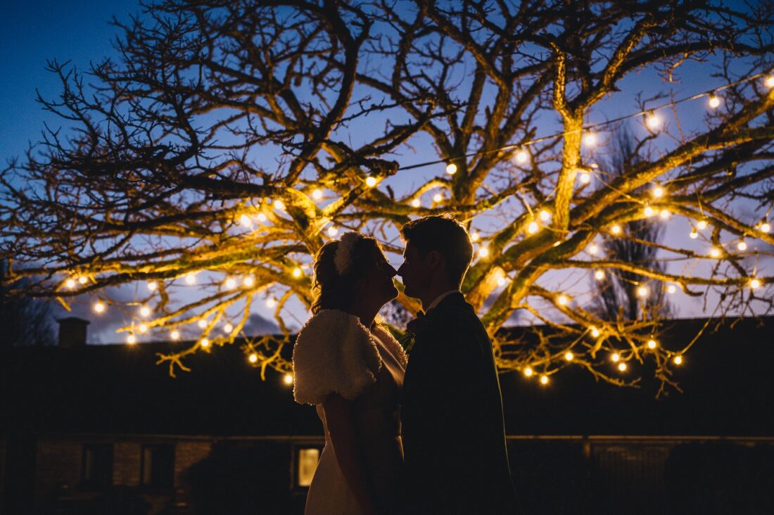 romantic winter wedding at Merriscout couple kissing and fairy lights lit on the tree during the blue hour